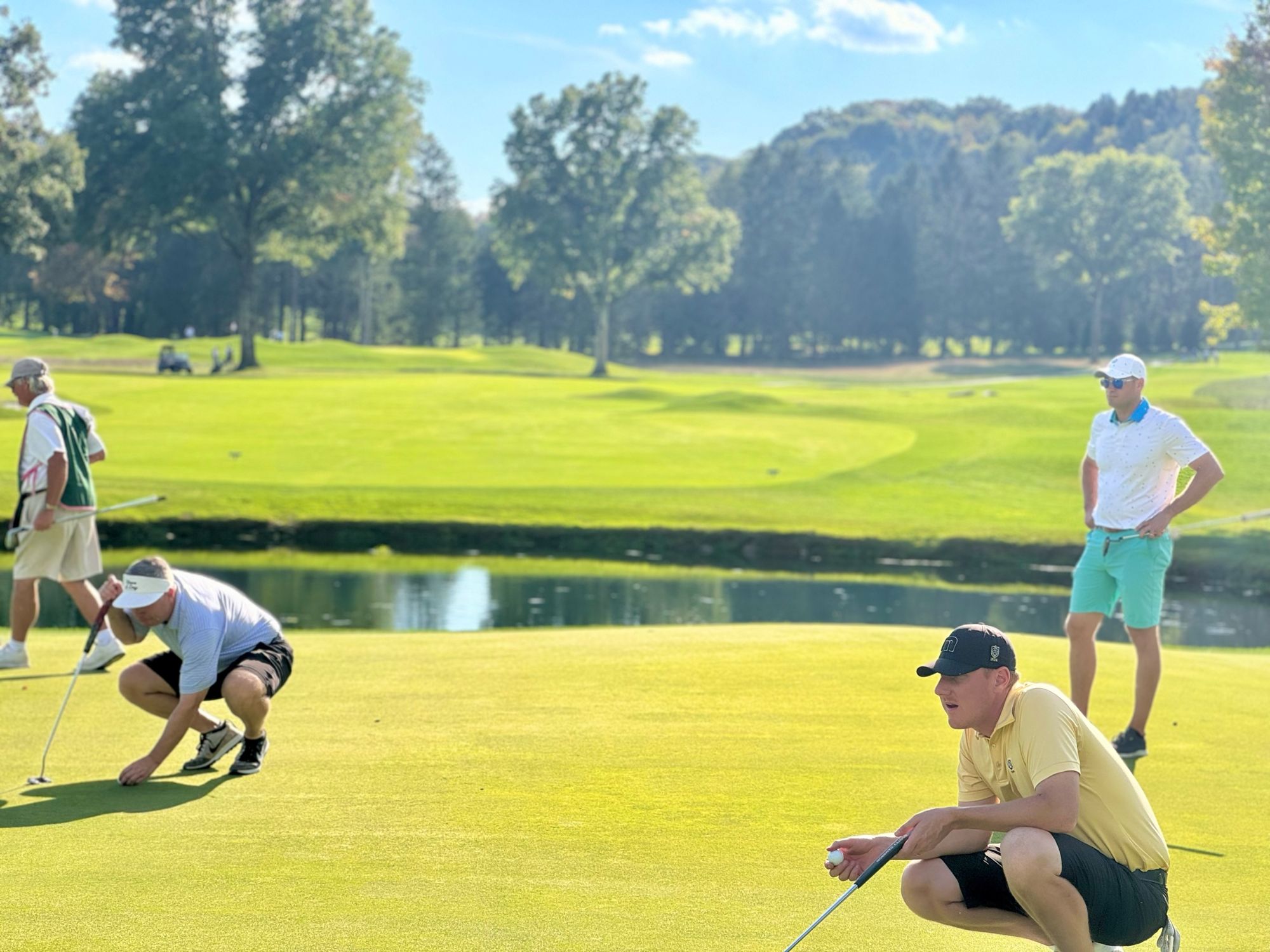 Players crouching to read a putt on the green while a teammate looks on